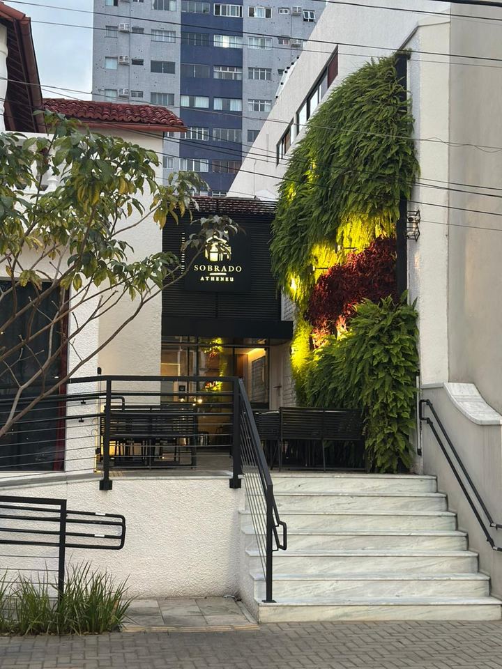 Fachada do Sobrado Atheneu, em Natal: escada de mármore, jardim vertical com samambaias e a placa iluminada na entrada